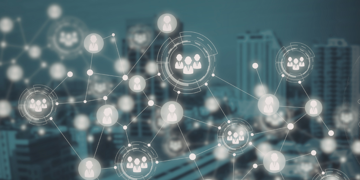 Grafika wyobrażająca sieć powiązań i relacji. Abstrakcyjna sieć linii łącząca jasne ikony przedstawiające sylwetki ludzi oraz grupy osób. Niektóre elementy są wyróżnione cyfrowymi okręgami przypominającymi interfejs analityczny. W tle widać rozmyte wieżowce w chłodnej, niebiesko-szarej tonacji.