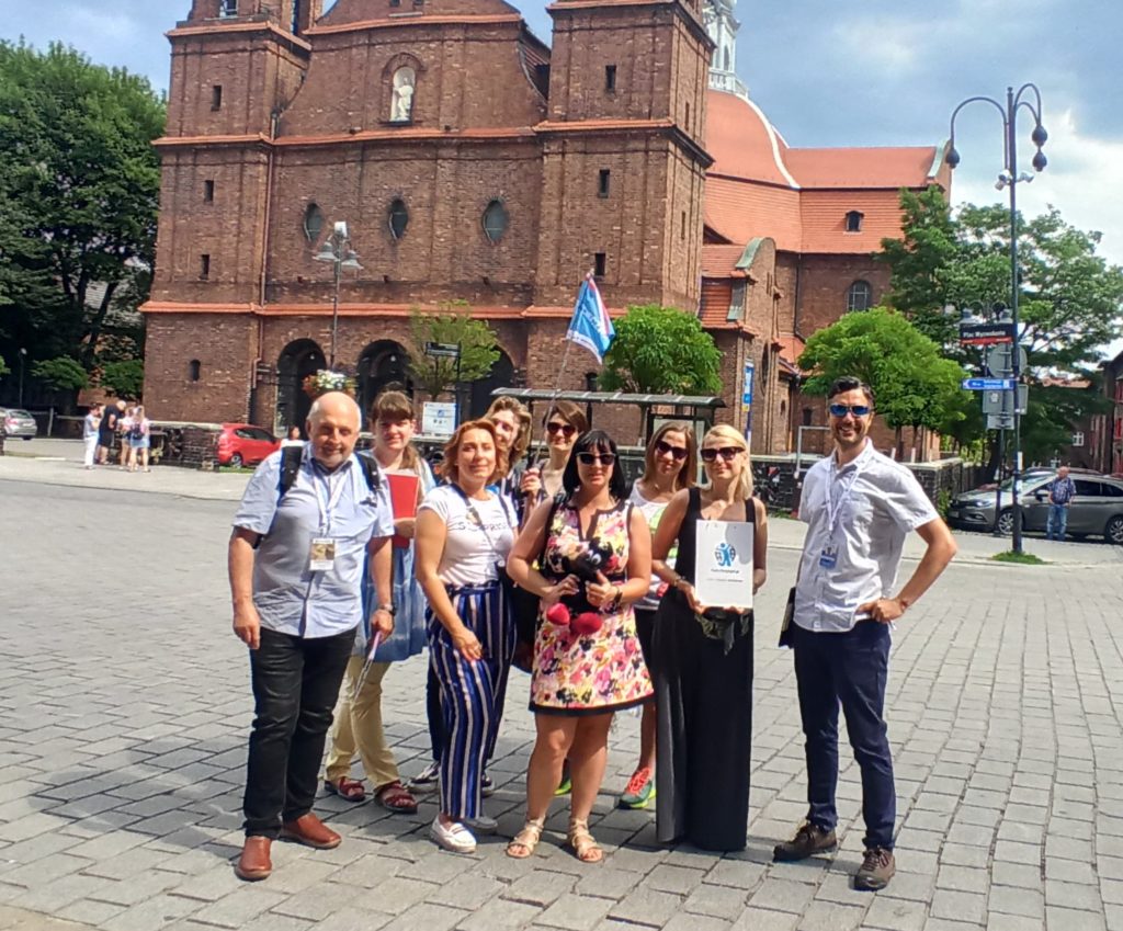 Grupa osób oznaczonych jako wycieczka na placu przed kościołem na osiedlu Nikiszowiec.