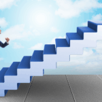 Mężczyzna w granatowym garniturze, trzymający teczkę, dynamicznie wbiega po schodach. Konstrukcja schodów ma kształt dużej, niebieskiej strzałki skierowanej ukośnie w prawy górny róg, na tle błękitnego nieba z chmurami. Ilustracja symbolizuje awans i dążenie do celu. Obrazuje rozwój kariery i sukces zawodowy.