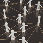Na ciemnym tle widoczne białe, trójwymiarowe figurki ludzi połączone siecią świecących. Jest to symboliczna ilustracja sieci kontaktów i współpracy.