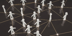 Na ciemnym tle widoczne białe, trójwymiarowe figurki ludzi połączone siecią świecących. Jest to symboliczna ilustracja sieci kontaktów i współpracy.