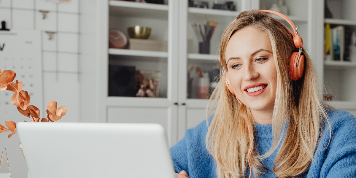kobieta w słuchawkach, siedząca przed otwartym laptopem, uczestnicząca w spotkaniu online