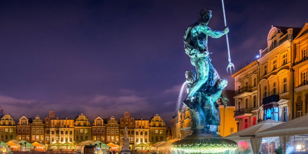 Nocny widok na rzeźbę Neptuna z trójzębem na tle kolorowych, zabytkowych kamienic poznańskiego Starego Rynku.