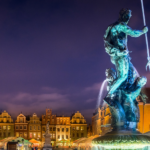 Nocny widok na rzeźbę Neptuna z trójzębem na tle kolorowych, zabytkowych kamienic poznańskiego Starego Rynku.