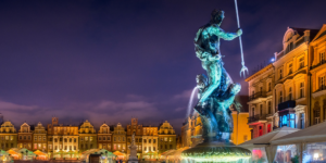 Nocny widok na rzeźbę Neptuna z trójzębem na tle kolorowych, zabytkowych kamienic poznańskiego Starego Rynku.