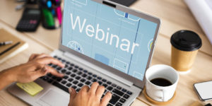 dłonie osoby piszącej na laptopie, na wyświetlaczu którego jest napis "webinar"