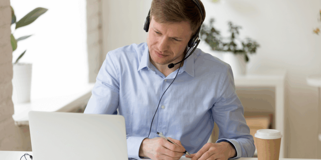 mężczyzna w słuchawkach przed laptopem robiący notatki w notesie