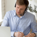 mężczyzna w słuchawkach przed laptopem robiący notatki w notesie